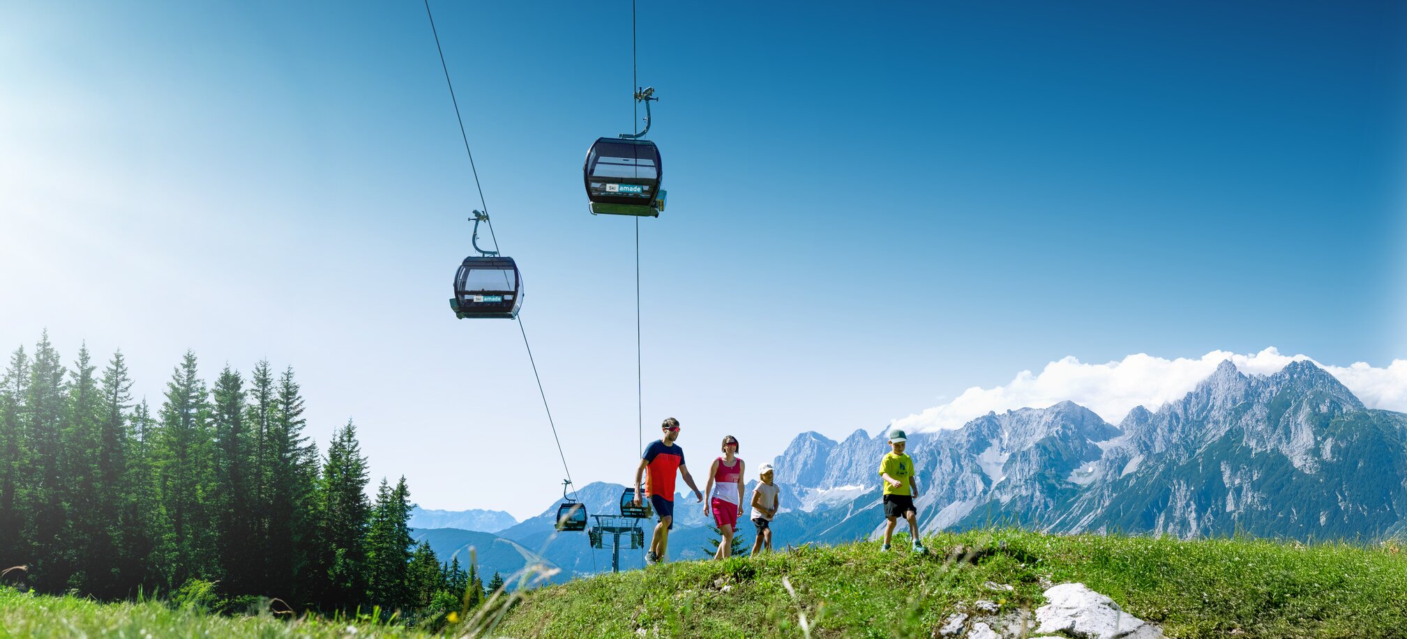 Family hiking on alpine meadow with gondola and mountain backdrop
